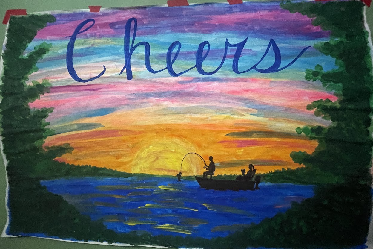 Hand-painted anniversary banner — a vivid sunset over a lake with two silhouetted figures fishing from a boat, brushed Cheers lettering across the sky, framed by painted green foliage
