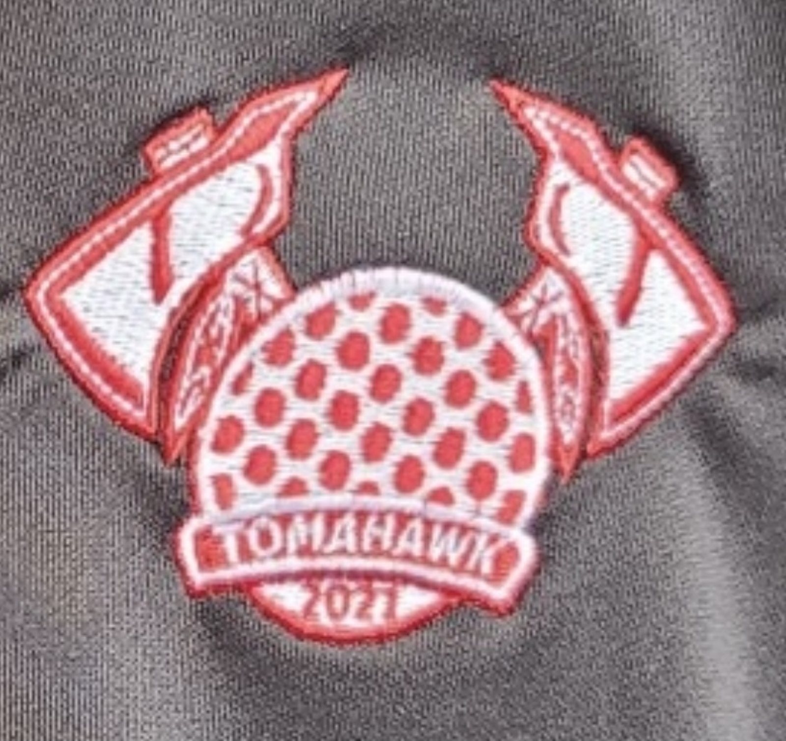 Close-up of the finished Team Tomahawk embroidery — red and white satin stitching forming the crossed axes, dimpled ball, and Tomahawk 2021 banner