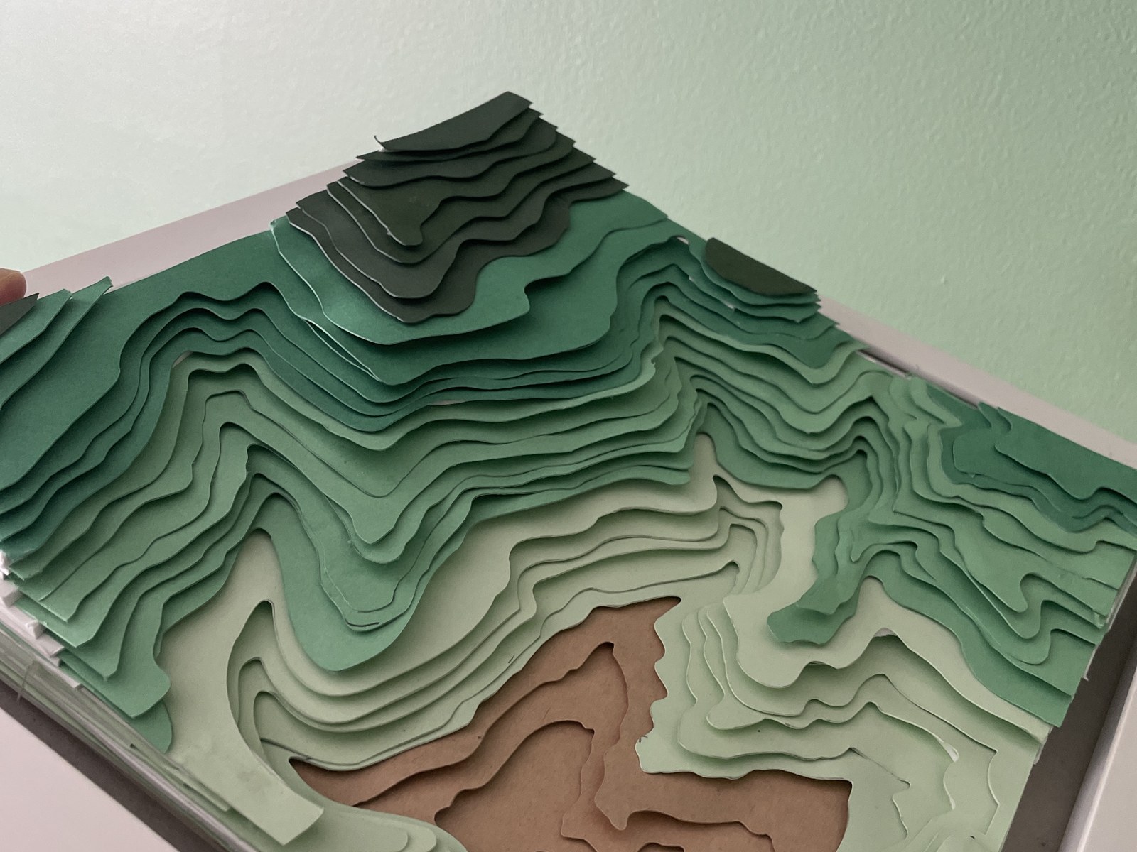 The finished shadowbox photographed at an angle, showing the stacked paper contour layers rising in relief